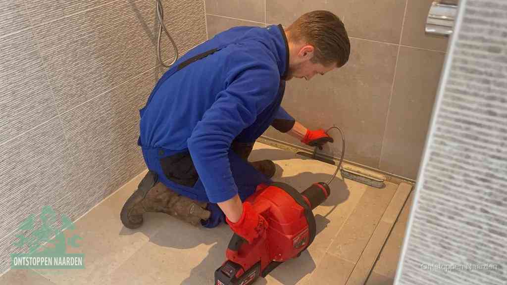 Een monteur ontstopt een langwerpige douchegoot met een elektrische veer, een doucheputje verstopt door haren en zeep in Naarden