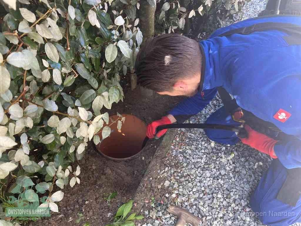 Een monteur voert een slang in een geopende rioolput in de tuin om het hoofdriool te ontstoppen in Naarden