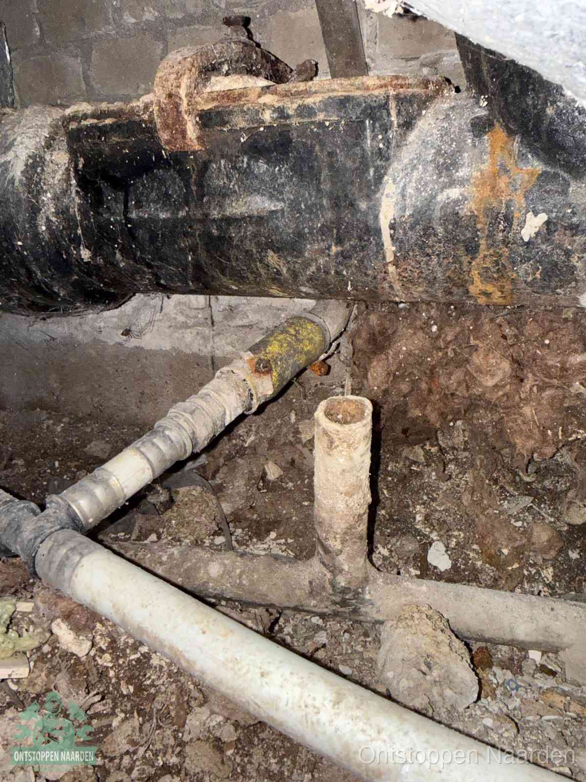 Een oude hoofdrioolbuis met roest- en kalkaanslag in een kruipruimte, oorzaak van terugkerende structurele rioolproblemen in Naarden